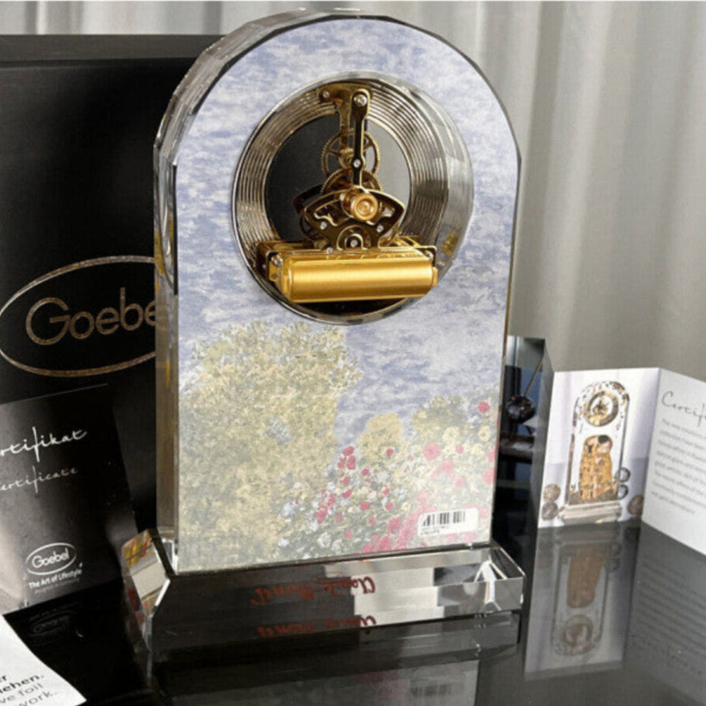 Decorative clock with gold interior and floral design on a reflective surface, with 'Goebe' branding.