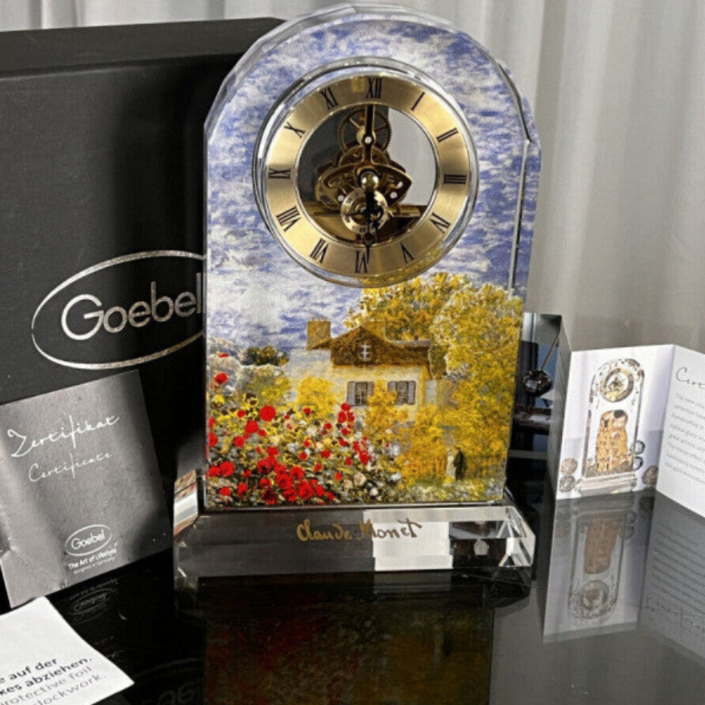 Decorative clock with floral design and 'Goebel' branding on a reflective surface.