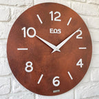 Rust-colored wall clock with 'EOS' branding on a white brick wall background