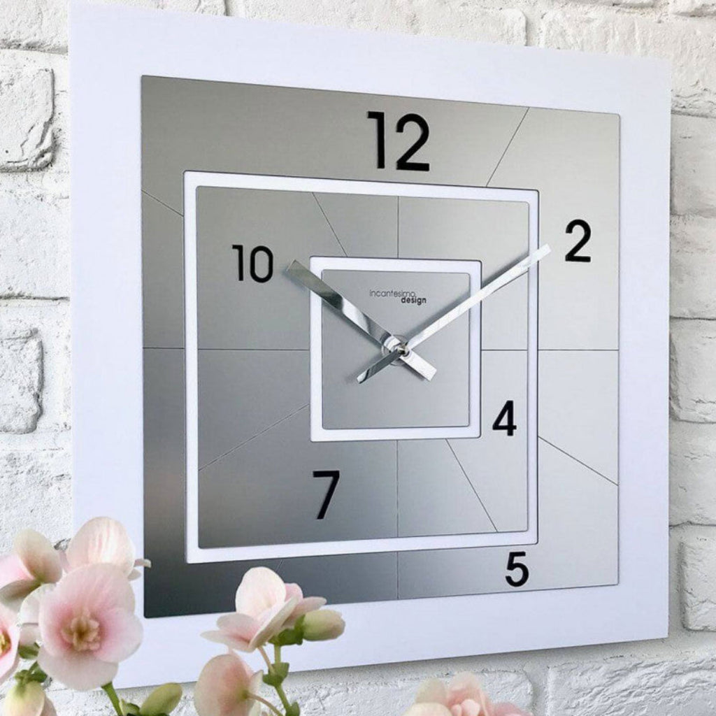 Square wall clock with white frame and gray face on a light brick wall.