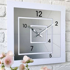 Square wall clock with white frame and gray face on a light brick wall.