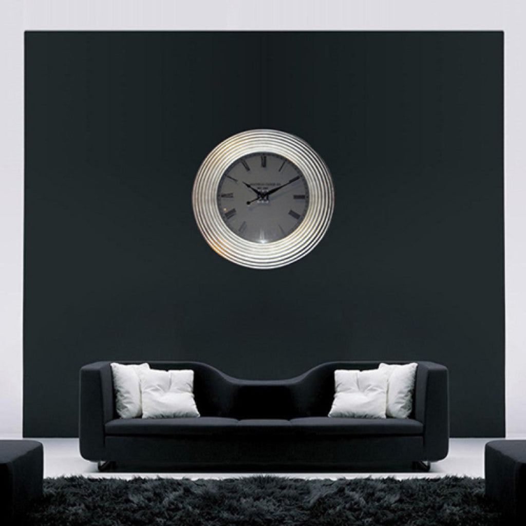 Modern wall clock on a black wall above a black sofa with white cushions.