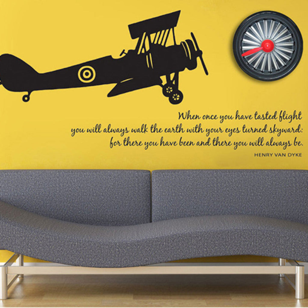 Wall with airplane decal, propeller graphic, and quote on a yellow background above a gray sofa.