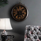 Decorative wall clock with intricate design on a gray wall, next to a floral armchair and lamp.