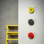 Three wall clocks in yellow, black, and red on a gray wall.