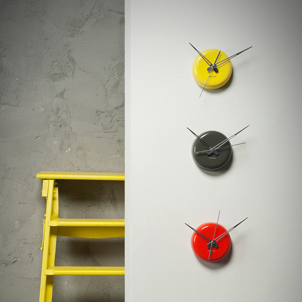 Three wall clocks in yellow, black, and red on a gray wall.