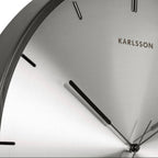 Close-up of a Karlsson wall clock with a metallic face and black hands.