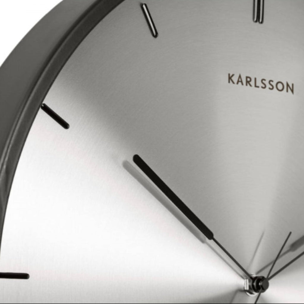 Close-up of a Karlsson wall clock with a metallic face and black hands.