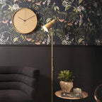 Decorative wall clock with floral wallpaper and a standing lamp in a room setting.