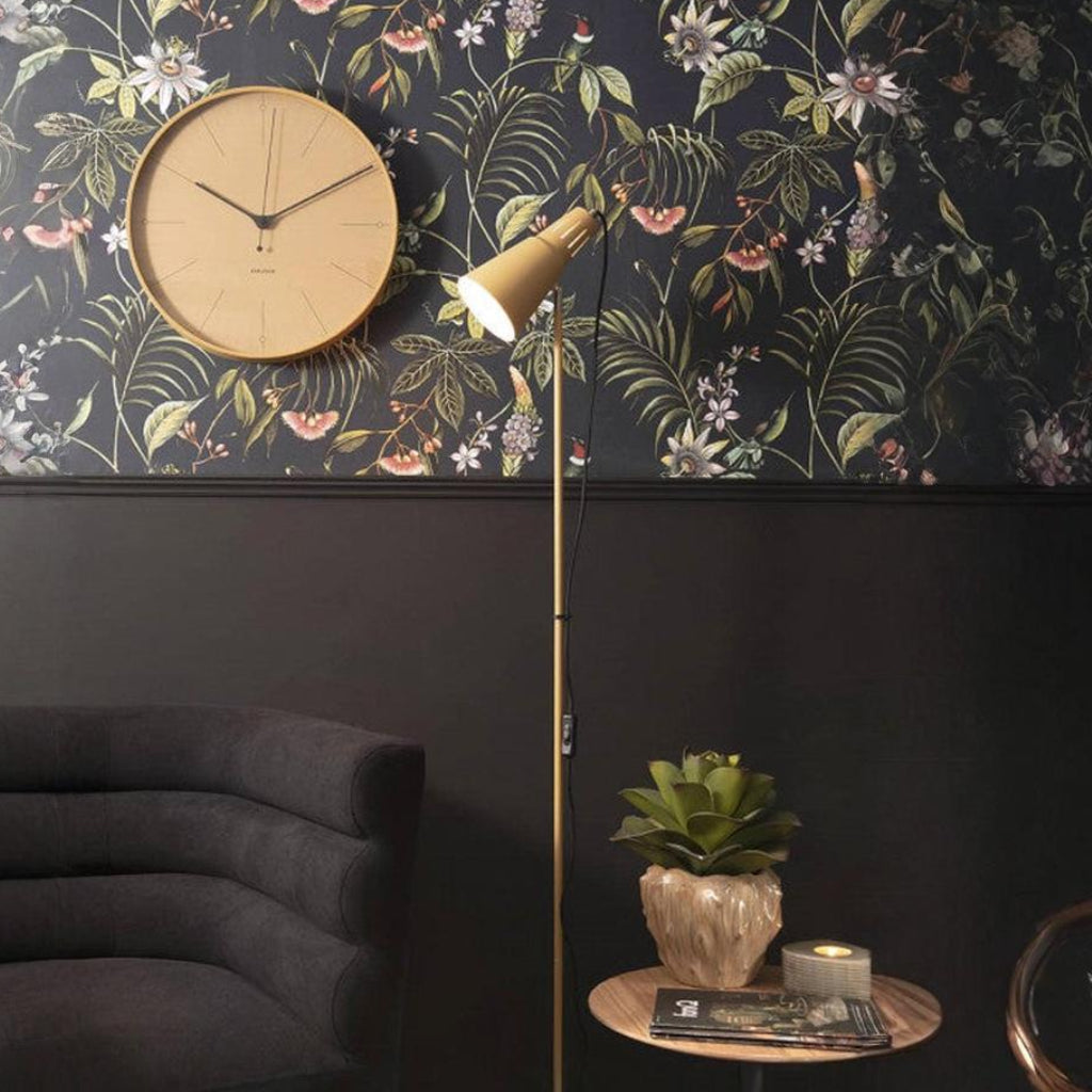 Decorative wall clock with floral wallpaper and a standing lamp in a room setting.