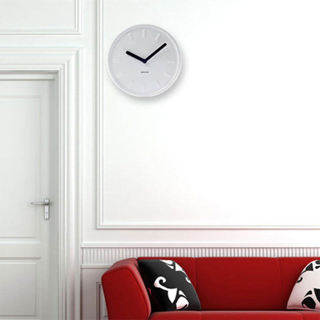 White wall clock on a white wall above a red sofa with black and white patterned cushions.