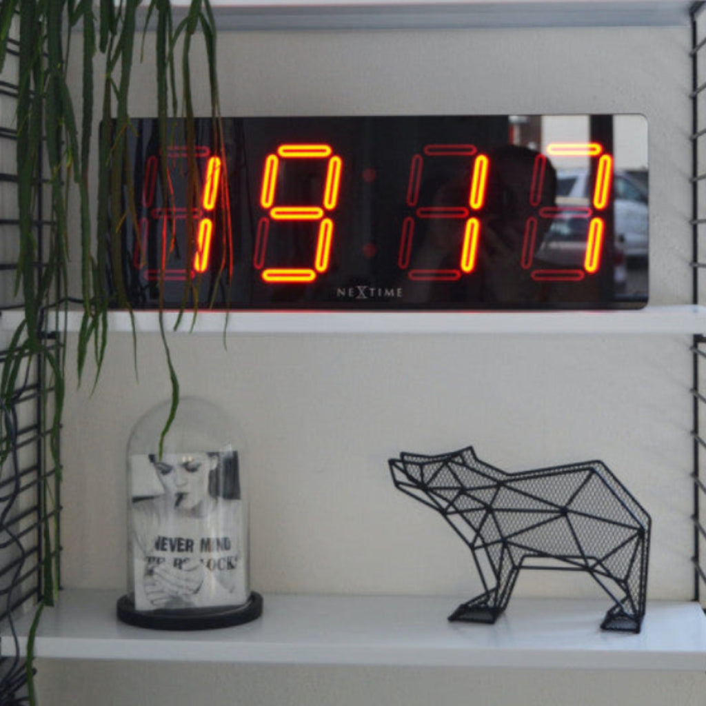 Digital clock displaying time on a shelf with decorative items