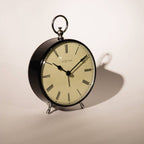 Round table clock with black frame and beige face on a light background