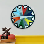 Colorful geometric wall clock on a white wall with books and a sculpture below.