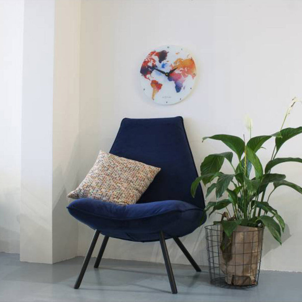 Navy blue chair with a patterned pillow in a room with a plant and a colorful wall clock.