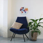 Navy blue chair with a patterned pillow in a room with a plant and a colorful wall clock.