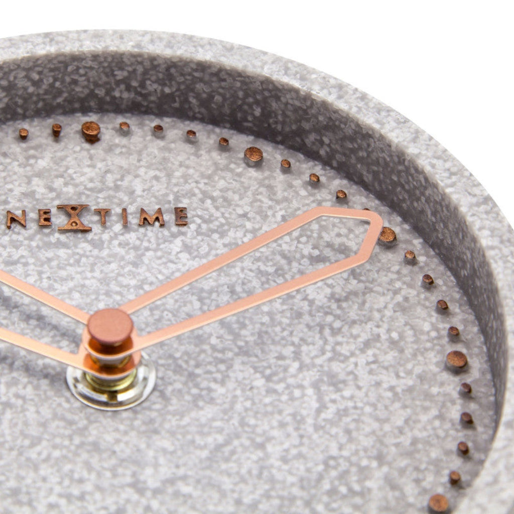 Close-up of a clock face with 'NeXtime' branding, featuring a textured gray surface and rose gold hands.