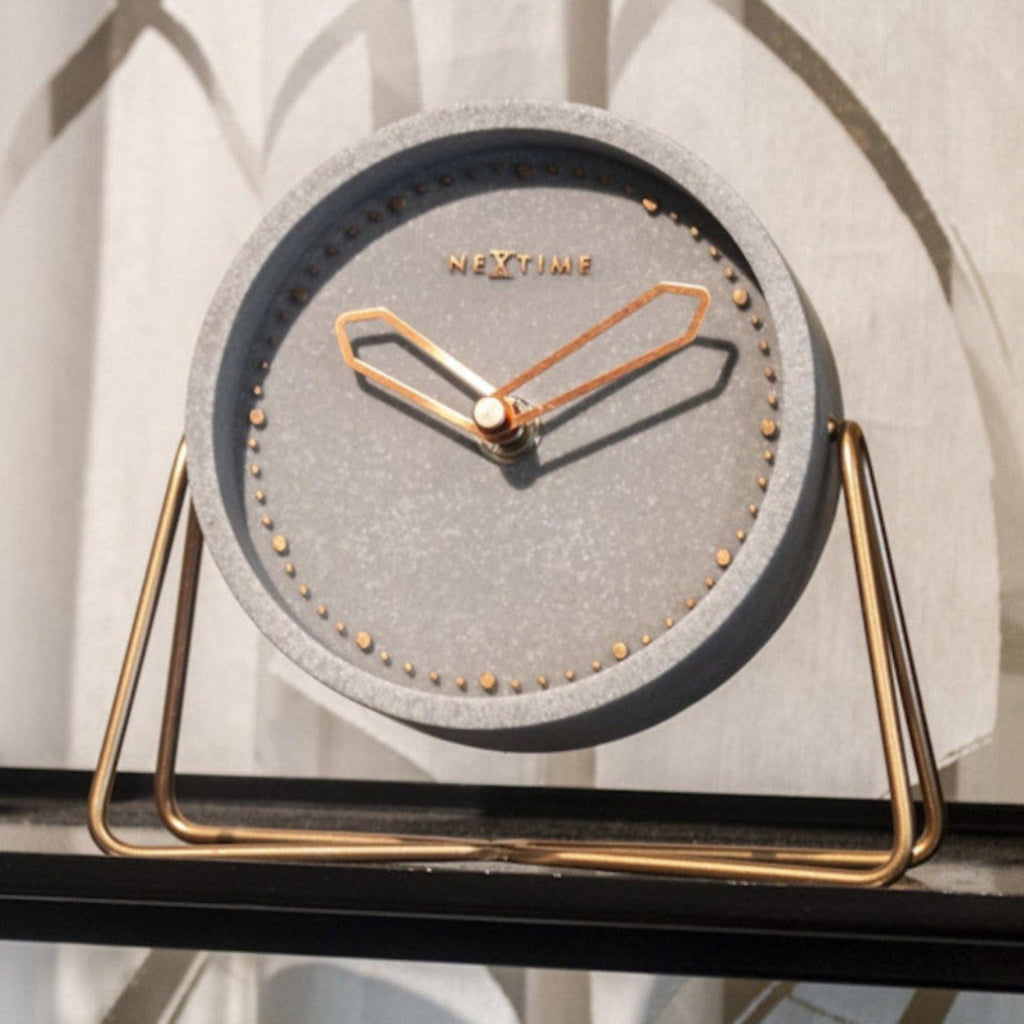 Table clock with gray face and gold frame on a white surface from Nextime available at Spacio retail stores in Mumbaii & Kolkata and online.