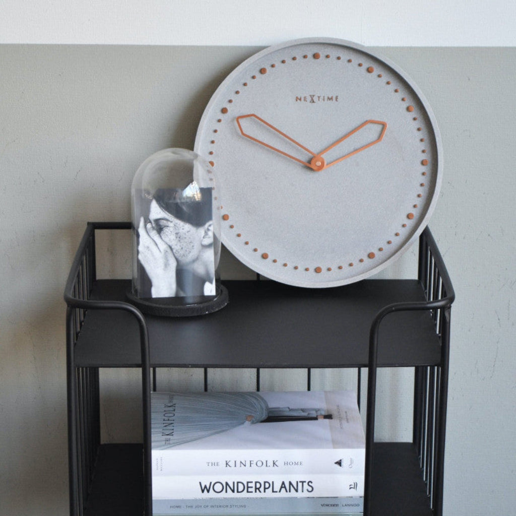 Round clock with copper accents on a black metal shelf against a white wall