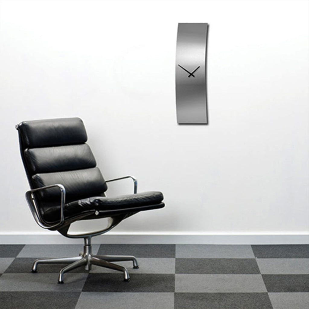 Modern black leather chair next to a silver wall clock on a white wall with a checkered floor.