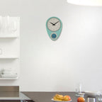 Teal wall clock on a white wall with a kitchen counter and fruit in the foreground.