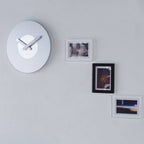 White wall clock on a light gray wall with framed pictures.