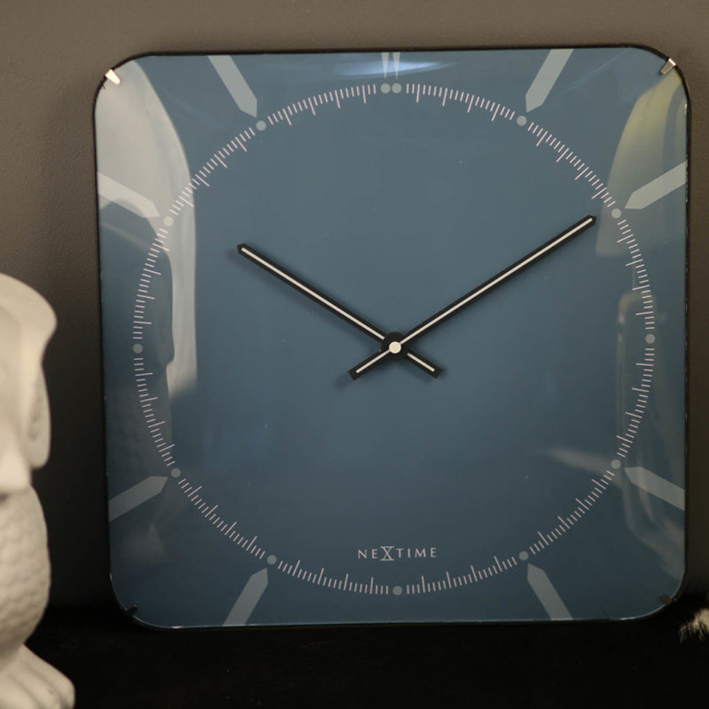 Square wall clock with black hands on a blue background, featuring the brand 'NeXtime'.