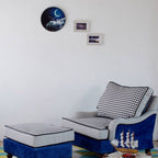 Chair and ottoman with decorative ship on a colorful rug against a white wall with framed pictures.