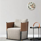 Modern armchair with brown leather accents and a matching side table against a light gray wall with a decorative clock.