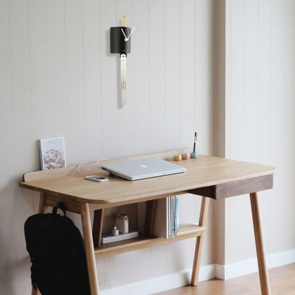 Wooden desk with laptop, books, and a backpack in a minimalistic room.