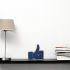Blue 'like' sign clock on a desk with a lamp and books in the background