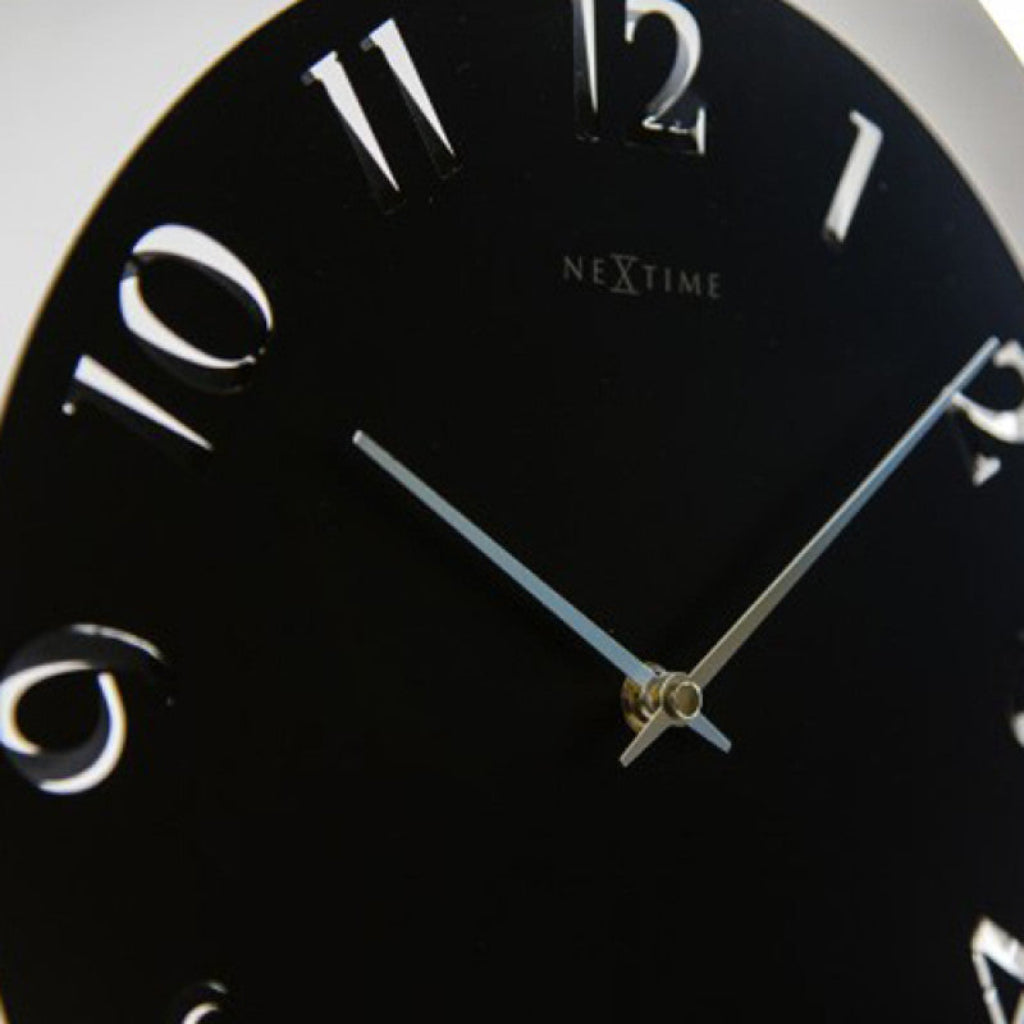 Close-up of a black clock face with white Roman numerals and 'Nextime' branding.