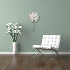 Modern interior with a white chair, vase of flowers, and wall clock on a light green wall.