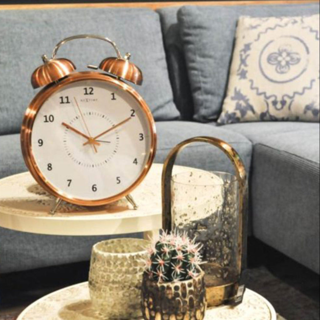 Copper alarm clock on a side table with a candle and cactus in a living room setting.