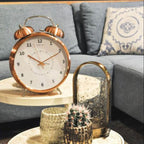 Copper alarm clock on a side table with a candle and cactus in a living room setting.