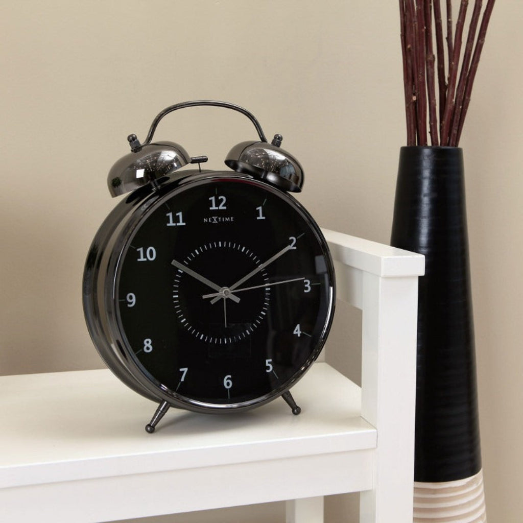 Black alarm clock on a white surface with a vase in the background
