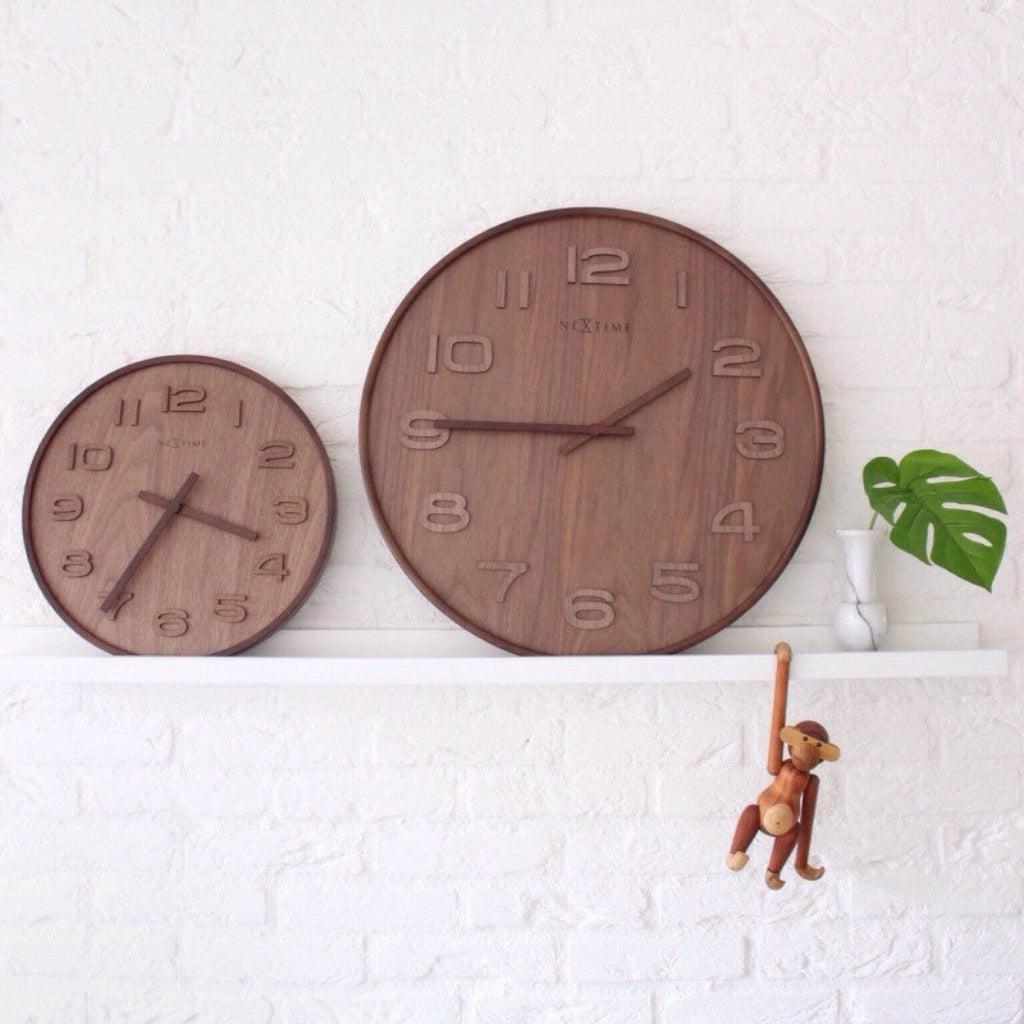 Two wooden wall clocks on a white wall with a small monkey figurine and plant.