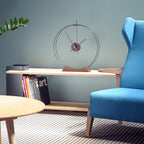 Modern living room with a blue armchair, wooden shelf, and decorative clock.