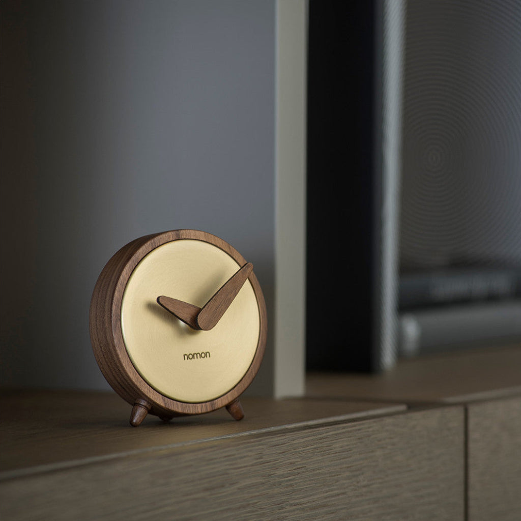 Wooden clock with beige face on a shelf against a dark background