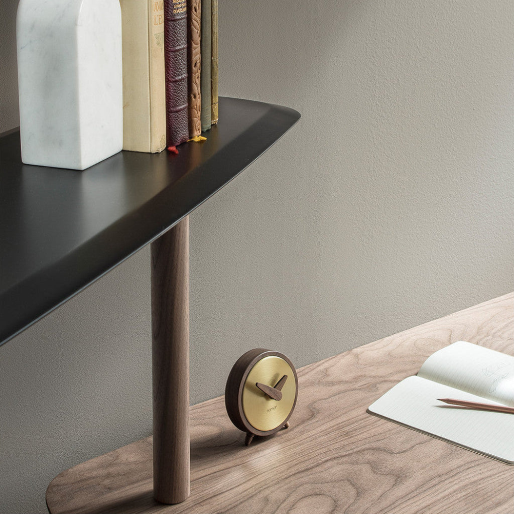 Small round clock on a wooden surface with a shelf in the background