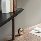 Small round clock on a wooden surface with a shelf in the background