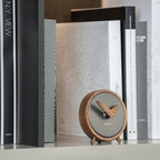Small round clock with wooden frame on a surface with books in the background