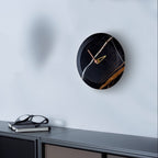 Modern wall clock with black and gold design on a light blue wall.