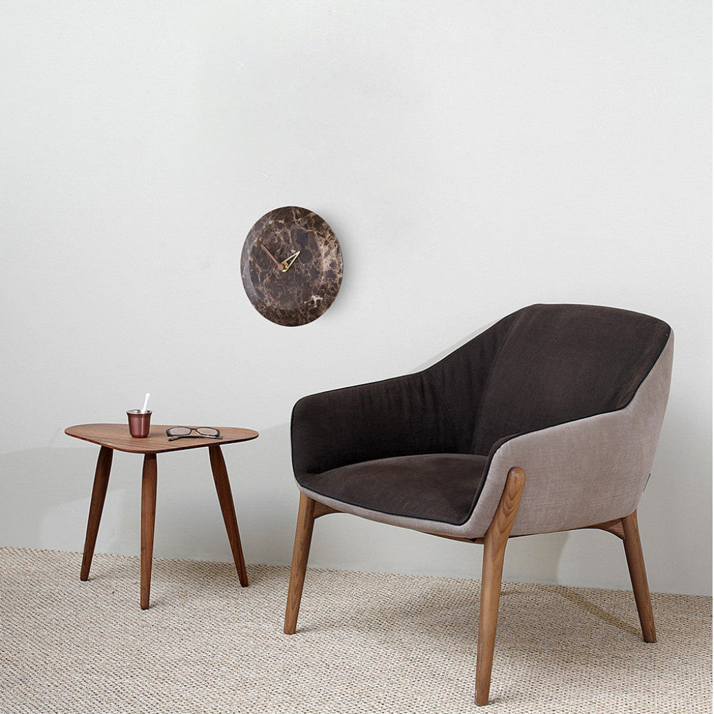 Modern armchair with wooden legs and a small round table against a white wall with a clock.