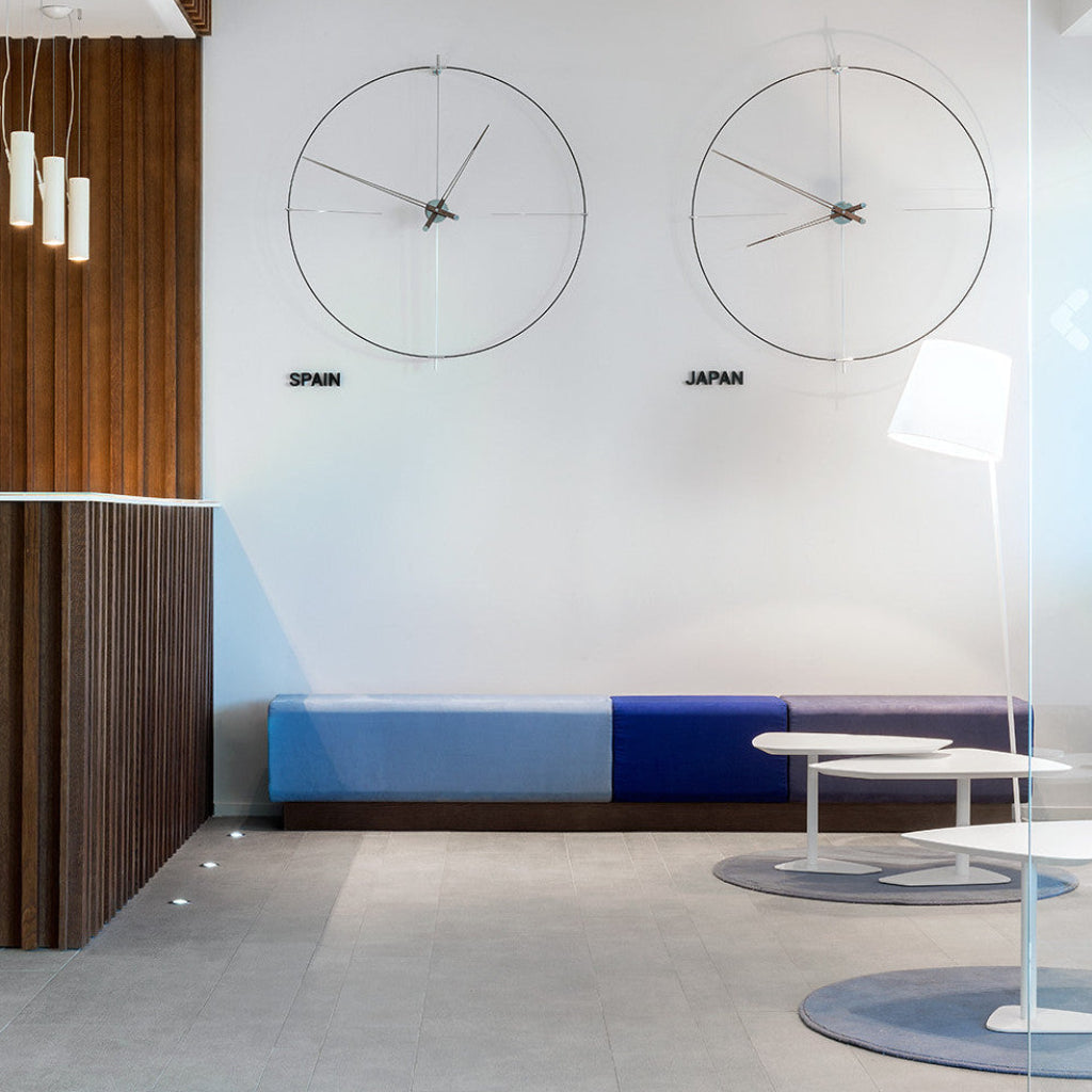 Modern interior design with two large wall clocks labeled 'Spain' and 'Japan', a blue bench, and minimal furniture.