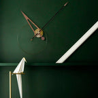 Modern wall clock with long thin design on a green wall, white floor lamp in foreground.