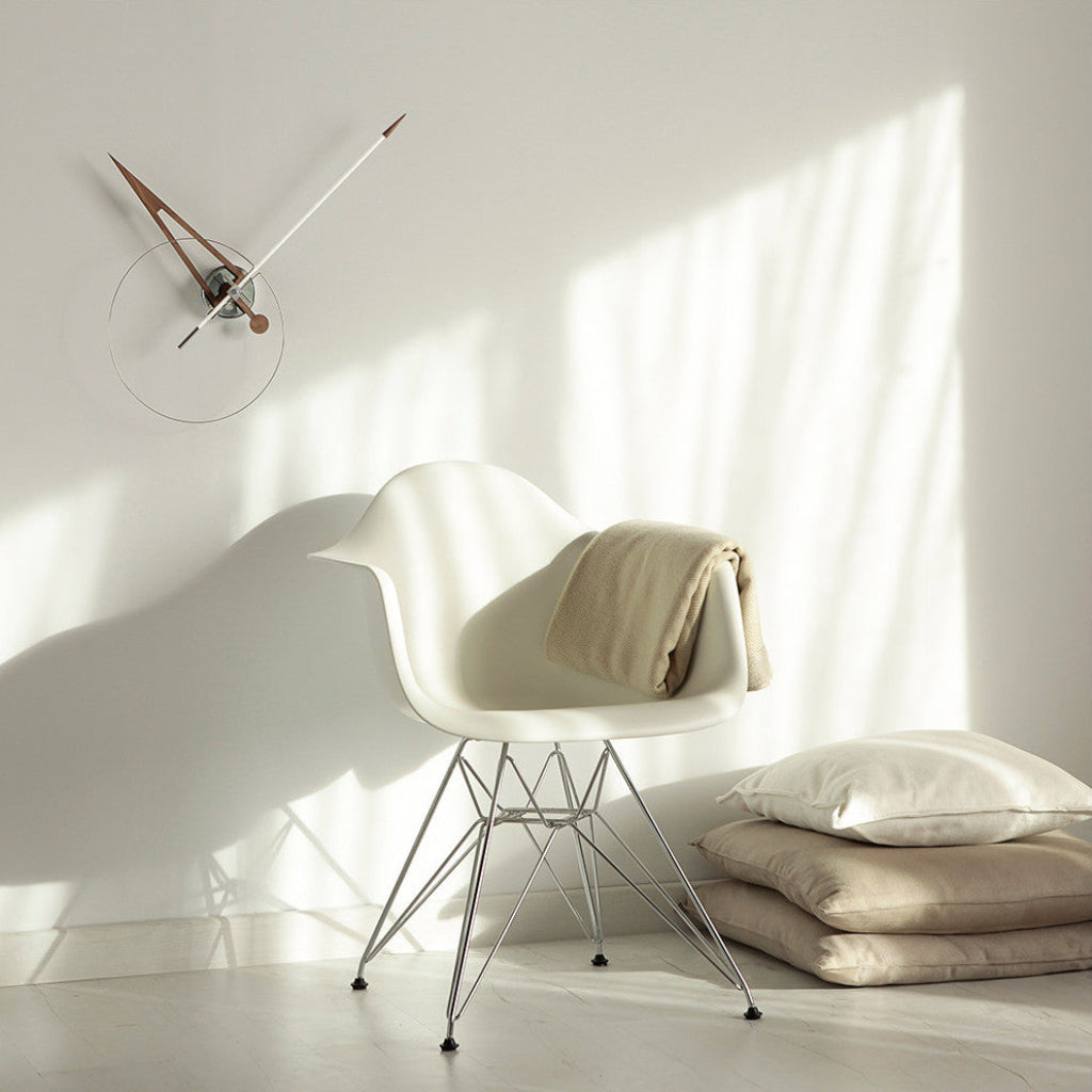 White chair with a beige blanket and pillows against a light wall with a clock.