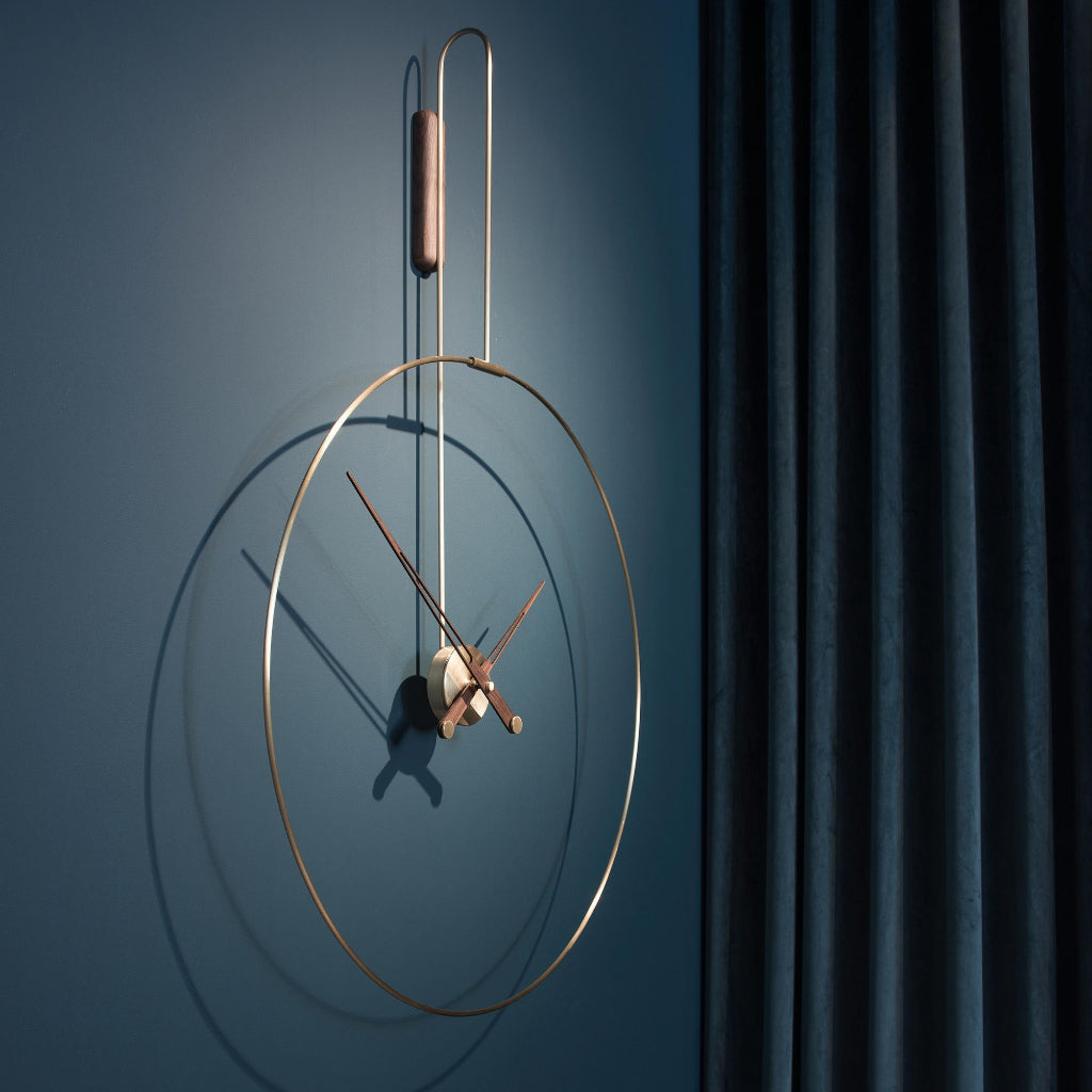 Modern wall clock with gold frame and bronze hands on a blue wall.