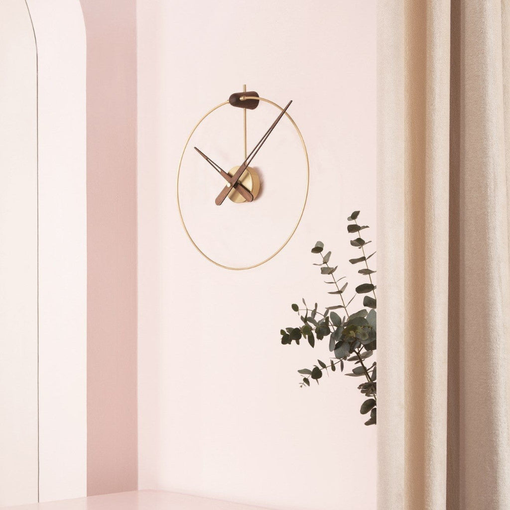 Modern wall clock on a light pink wall with a plant decoration.