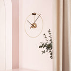 Modern wall clock on a light pink wall with a plant decoration.